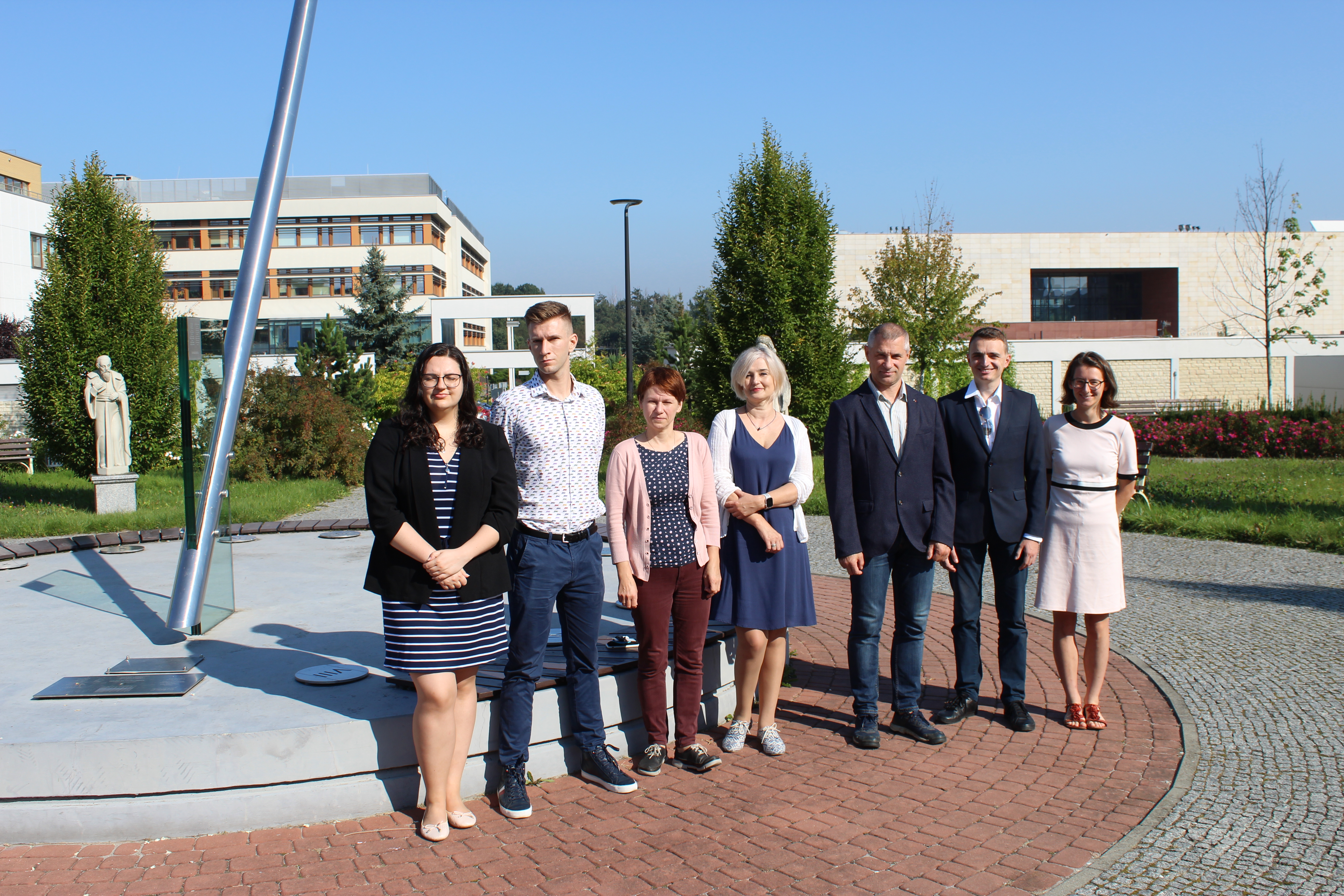 Photo of the members of the Metabolomics Laboratory, outside the building in a paved courtyard. Deciduous trees and other campus buildings in the background.